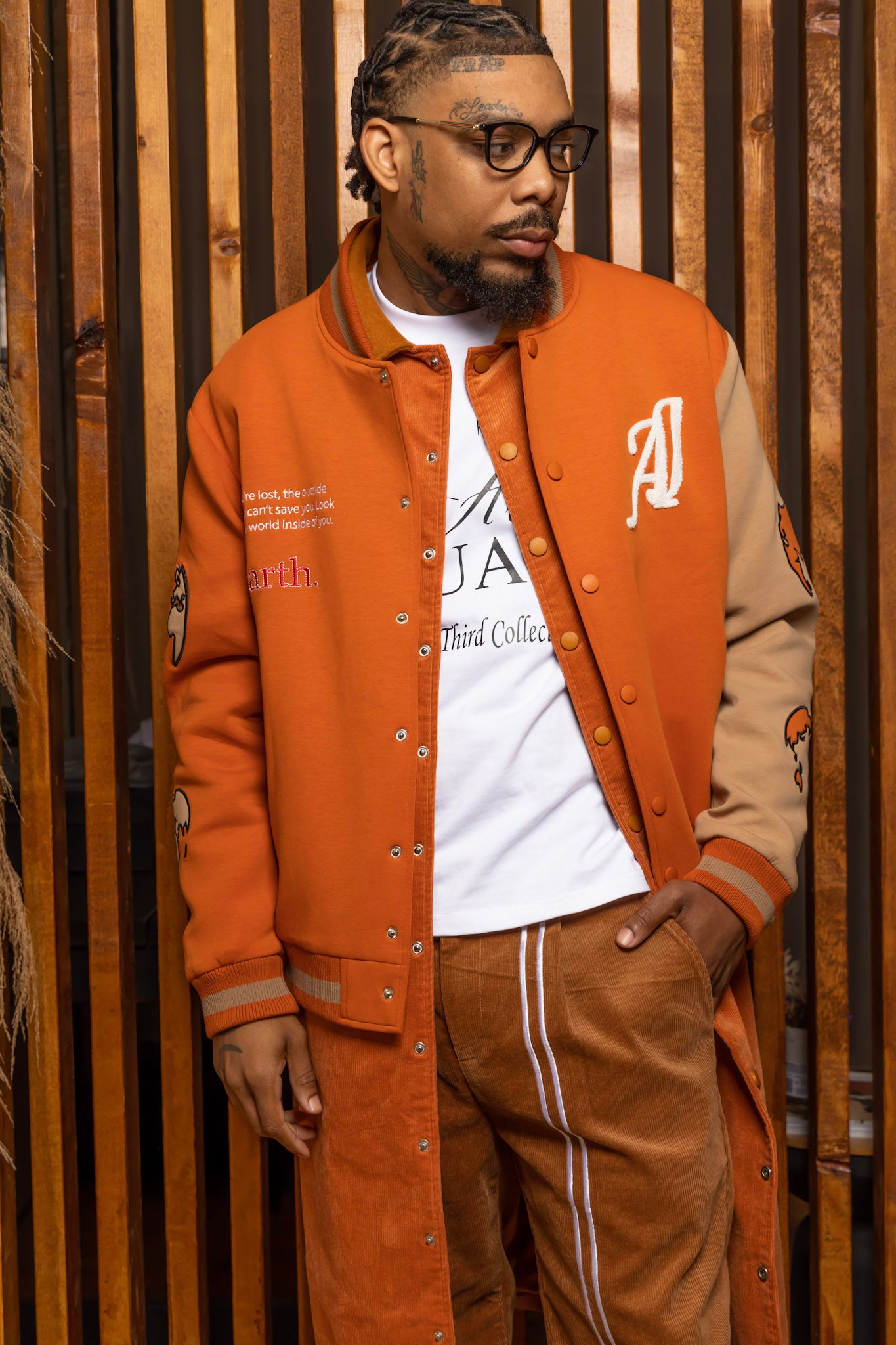 Model wearing Burnt Orange Worldly Letterman Jacket, Burnt Orange Corduroy Trench Coat, Tan NY vs NY Pants, The Third Collection T-Shirt: White in a Arius Juan Campaign.