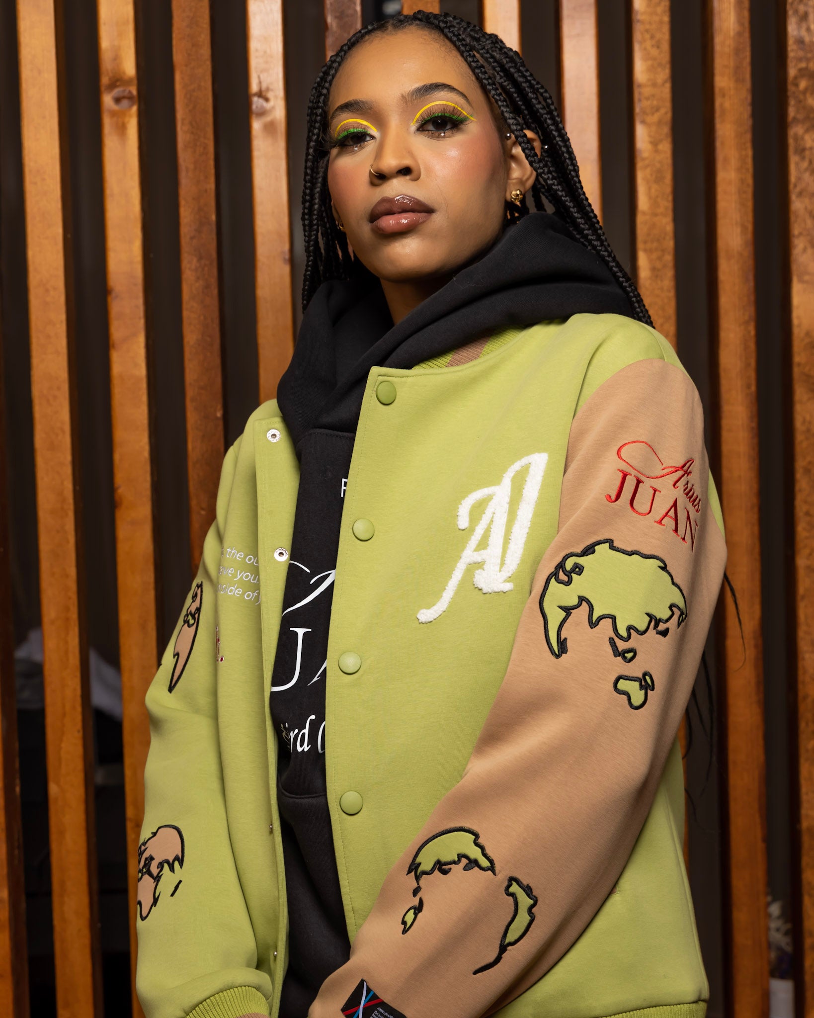 Model wearing Olive Green Worldly Letterman Jacket, The Third Collection Hoodie: Black, Nature's Gift Olive Green Pants in a Arius Juan Campaign.